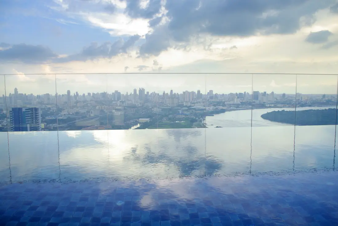 Piscina de borda infinita na cobertura, com a cidade e o céu refletidos na água.